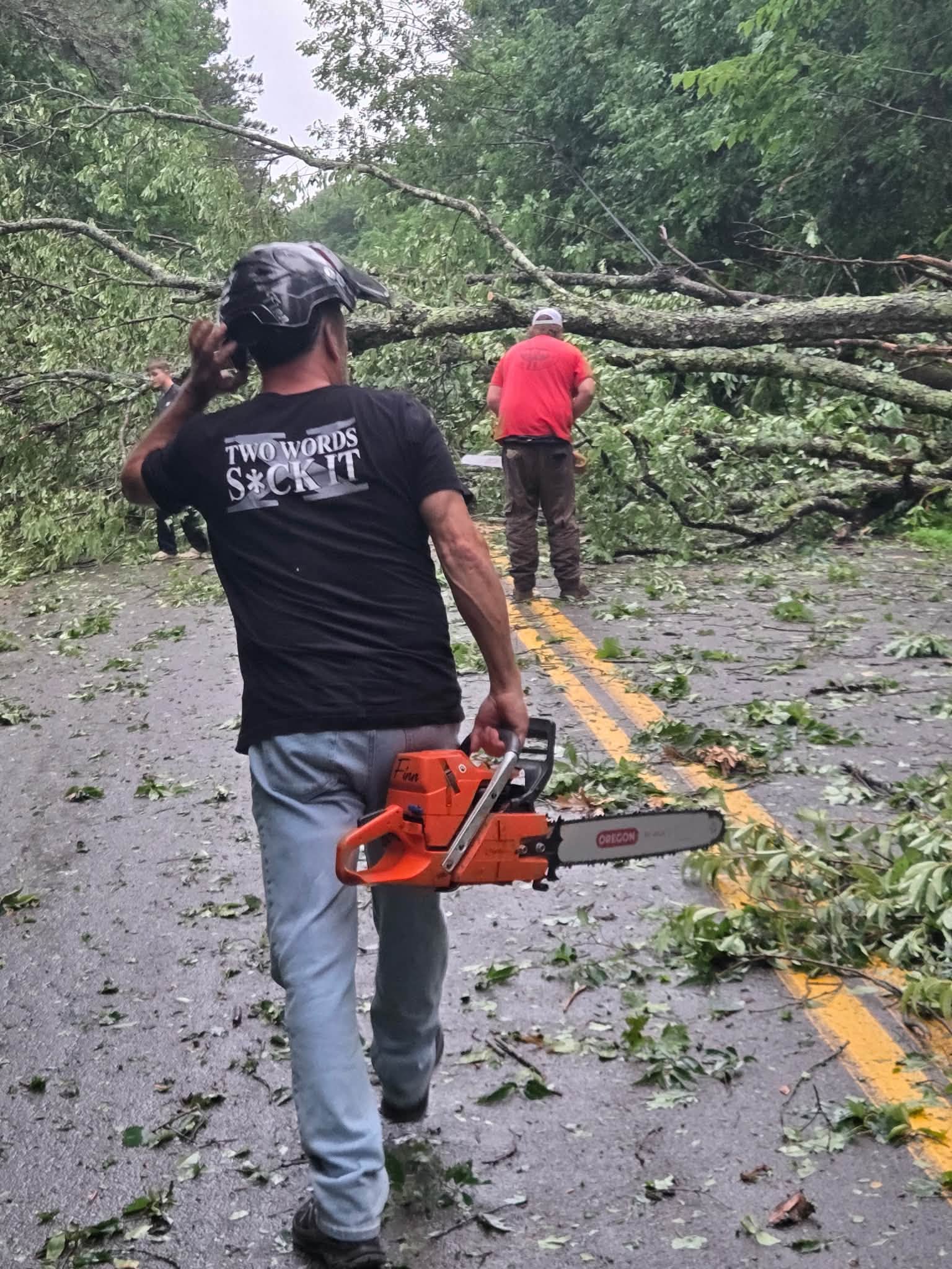 Crew member carrying a chainsaw toward a tree down over the road